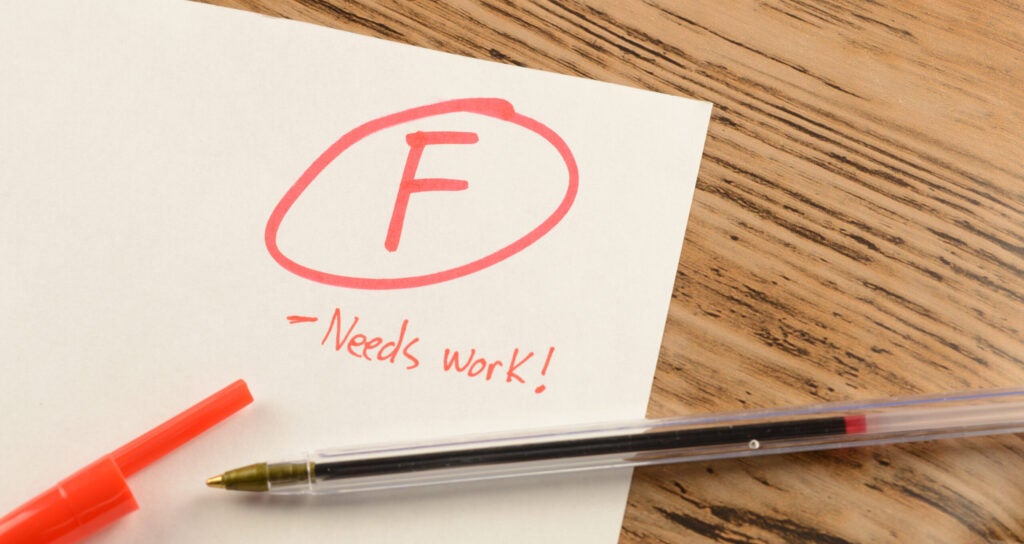 The corner of a white school paper with a circled F and "Needs Work!" written in red.