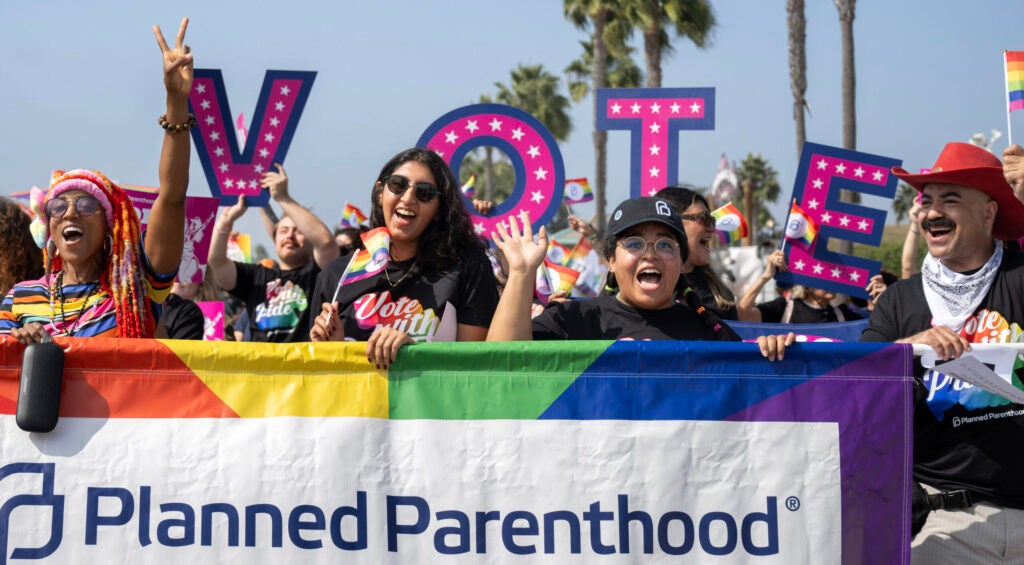 Three women and a male carry a Planned Parenthood banner ringed in rainbow colors during the Orange County Pride Parade in 2024.