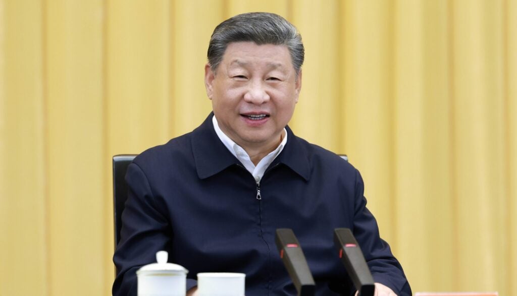 A smiling Chinese Chairman Xi in dark blue jacket in front of gold curtains.