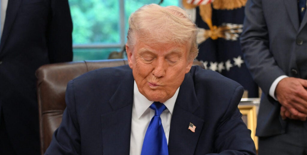 President Trump, his mouth humorously askew, looks down toward his desk.
