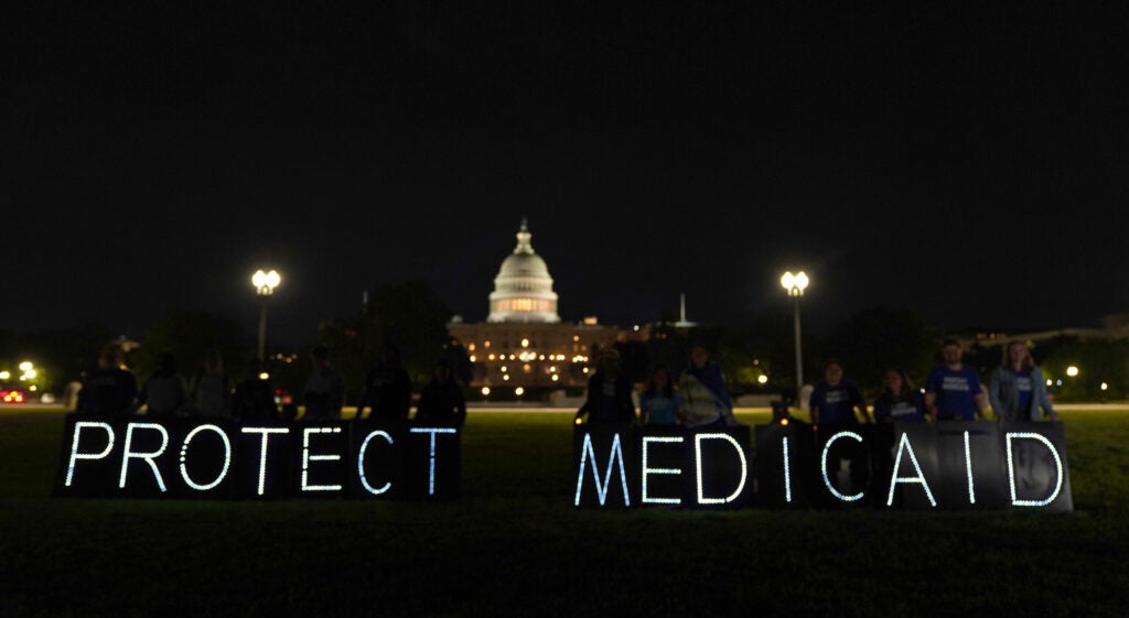 White lights spelling out "Protect Medicaid" are lit in front of the U.S. Capitol at nighttime.