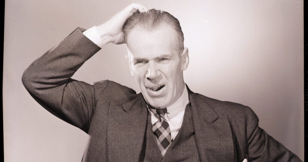 Man in a suit scratches his head quizzically in an old black and white photograph