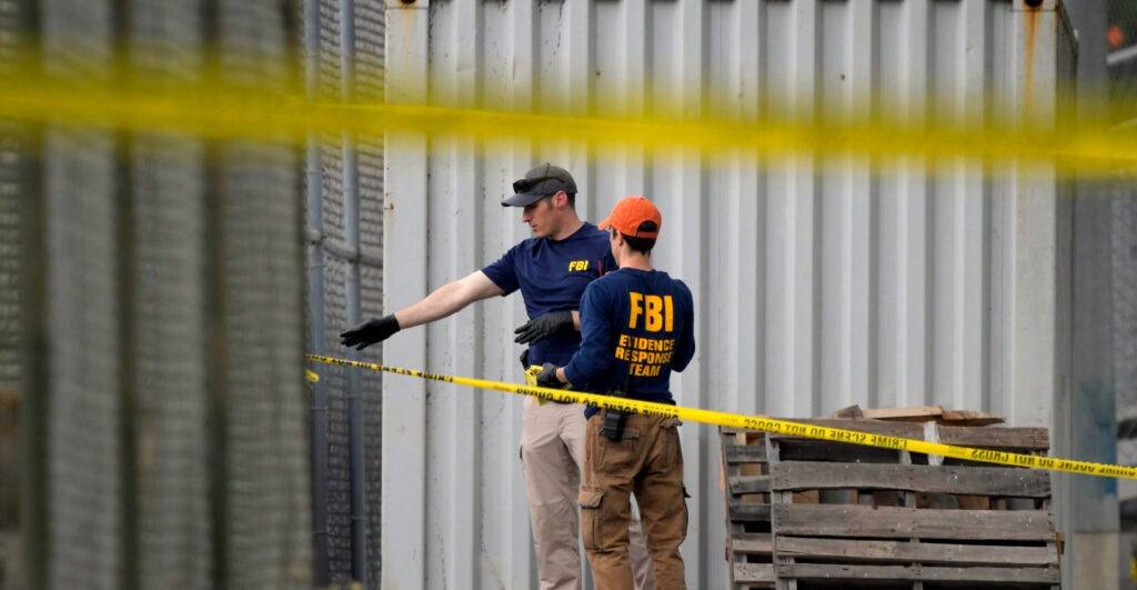 Two FBI agents examine scene of 2017 Congressional Baseball Game shooting, behind two strands of police tape