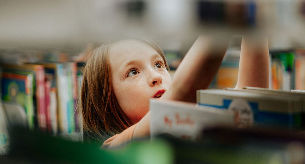 A young girl looks at a book with wide eyes in a library