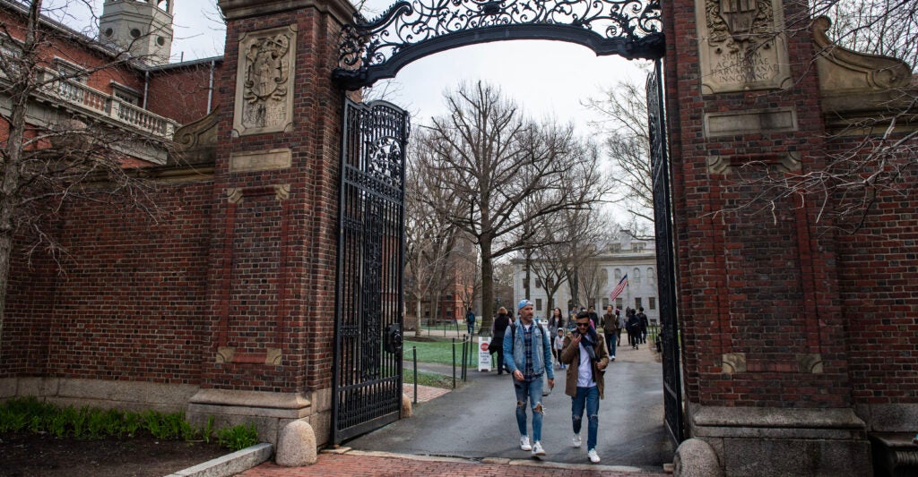 People walk through a large brick and iron gate as they exit Harvard Yard on the campus of Harvard University