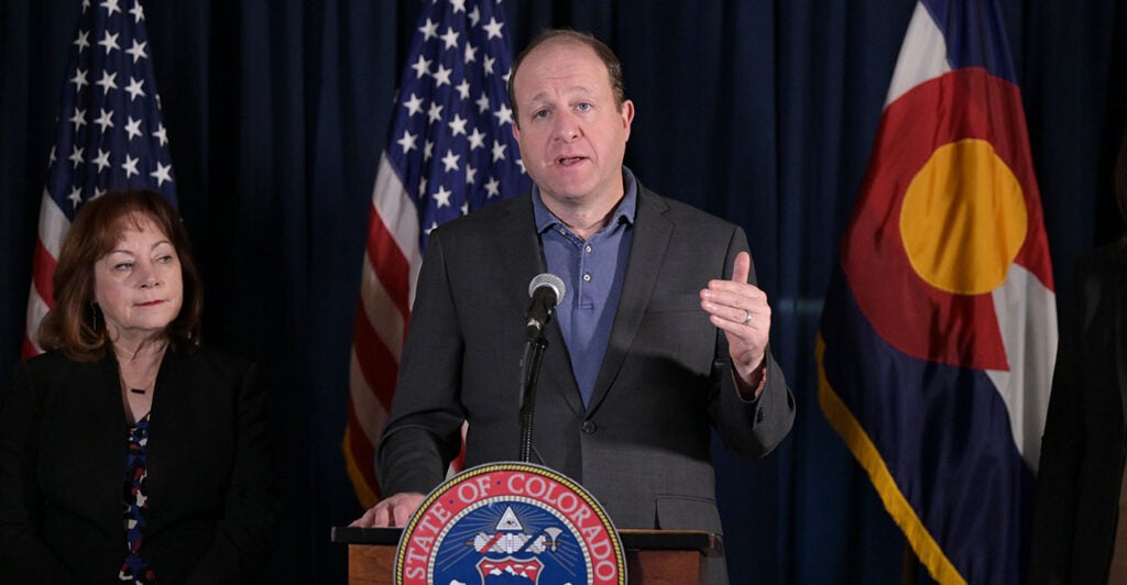 Jared Polis in a suit behind the seal of the state of Colorado