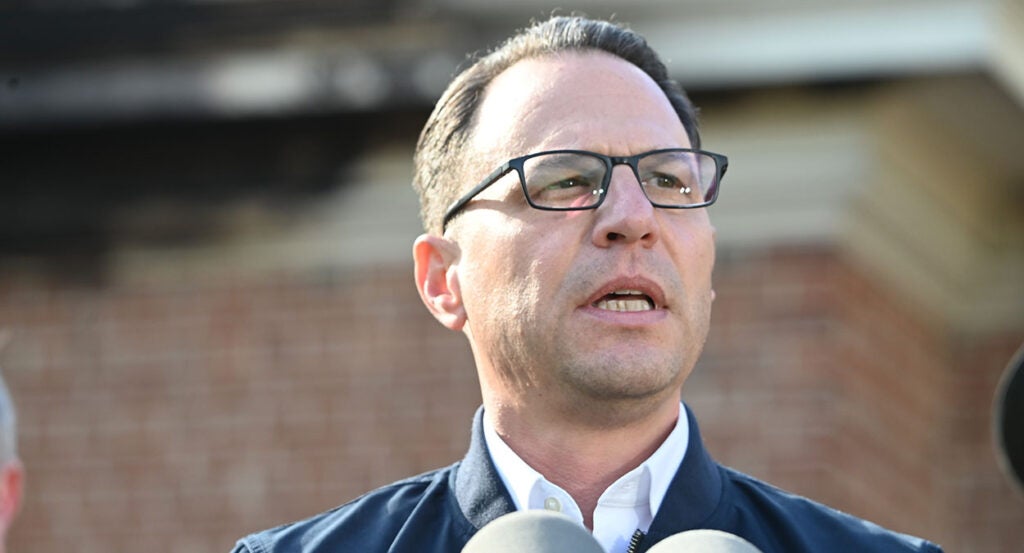 Josh Shapiro in a suit in front of a brick building.