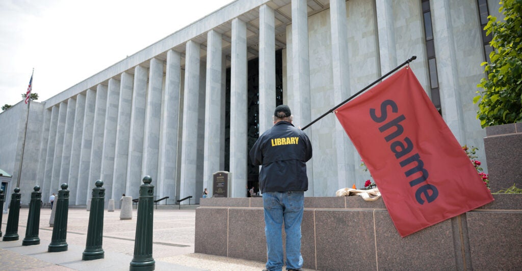 A man holds a red flag that reads "Shame" outside the Library of Congress on May 12 in Washington, D.C. Days earlier, President Donald Trump had fired Carla Hayden as the head of the Library of Congress.