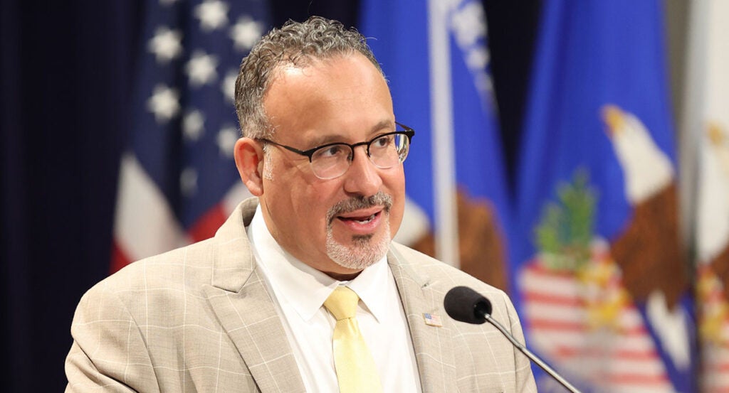 Miguel Cardona in a checkered suit with a yellow tie