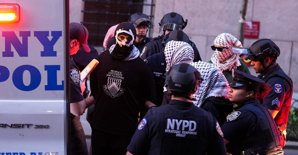 Police officers move protesters into a police vehicle.