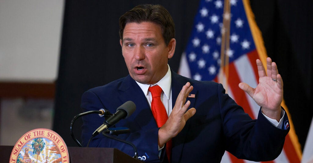 Florida Gov. Ron DeSantis in a blue suit with a red tie and an American flag pin