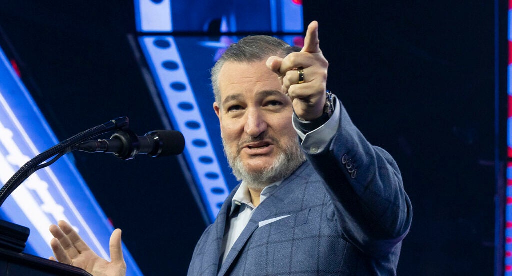 A smiling Ted Cruz in a checkered suit points.