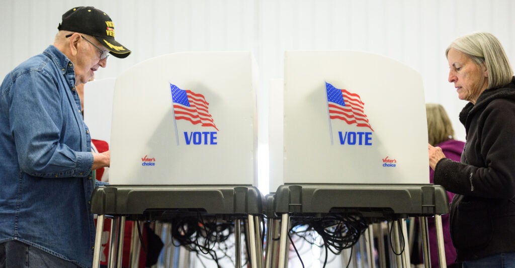 An older male and female vote in face-to-face-voting booths.