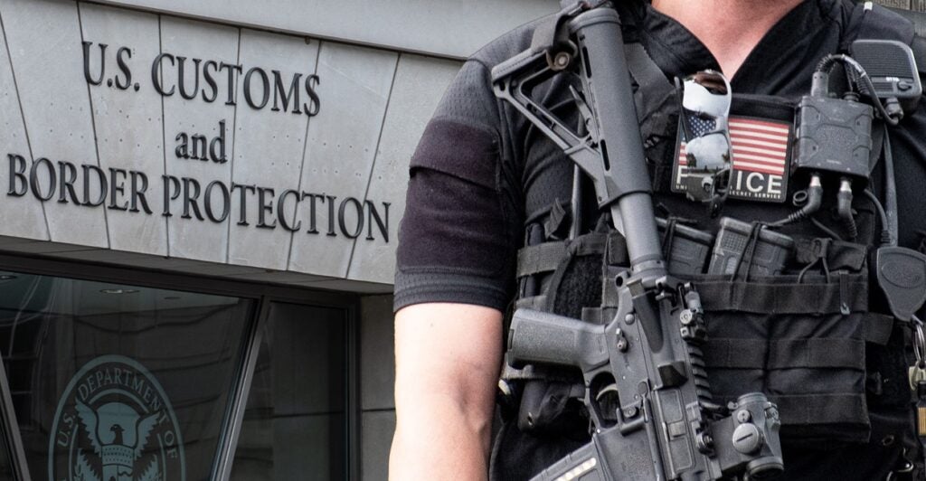 An armed U.S. Customs and Border Protection agent stands outside with a gun strapped to him.