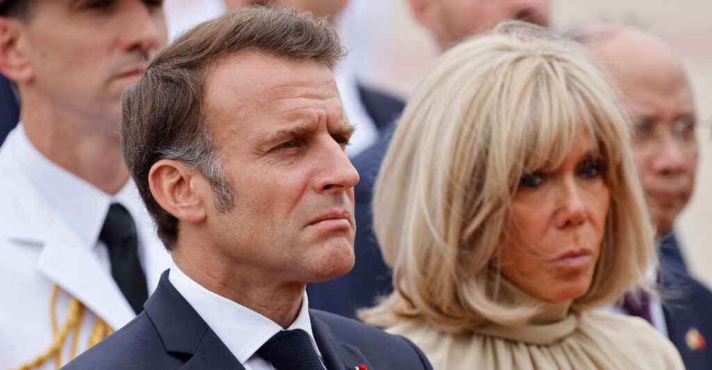 Close-up of French President Emmanuel Macron and wife Brigitte looking dour while seated in a crowd.