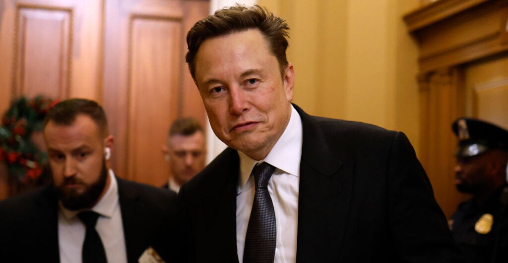 DOGE head Elon Musk in a black suit and tie walking through the halls of Congress