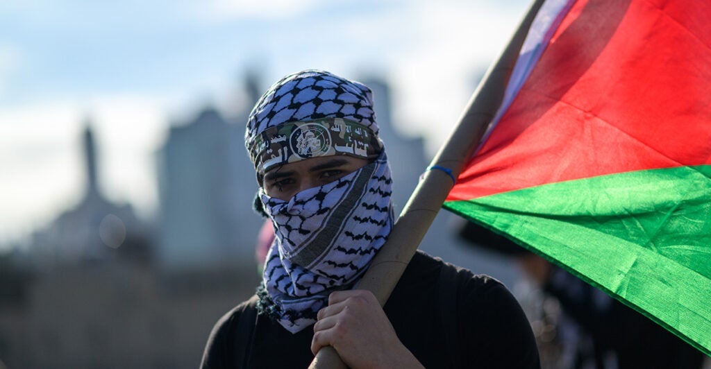 An anti-Israel activist demonstrates in New York City, wearing an identity-concealing, Arabic-style headdress and carrying a Palestinian flag.