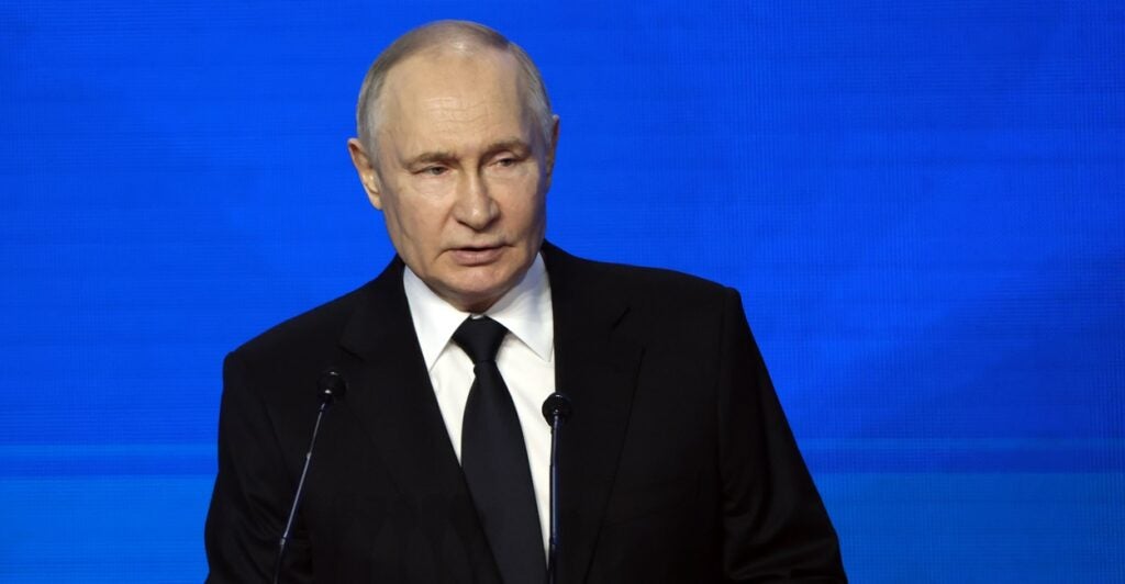 Vladimir Putin stands at a podium and looks out onto the crowd.