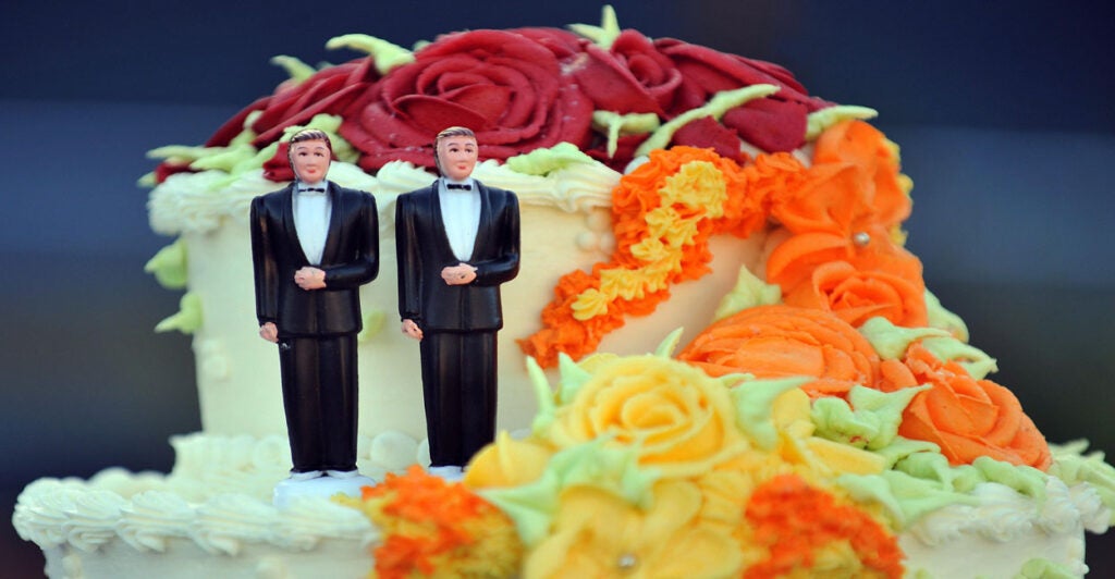 A colorful wedding cake for a same-sex marriage, with two male figurines in tuxes.
