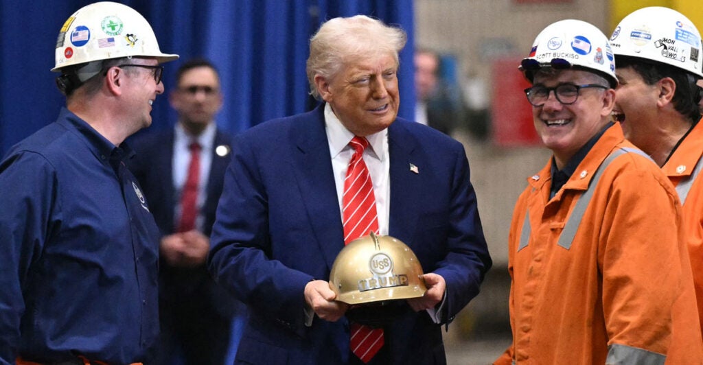 Donald Trump, gold hard hat in hand, jokes with three steel workers.