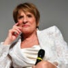 Actress Patti LuPone sitting in a white dress looking stern.