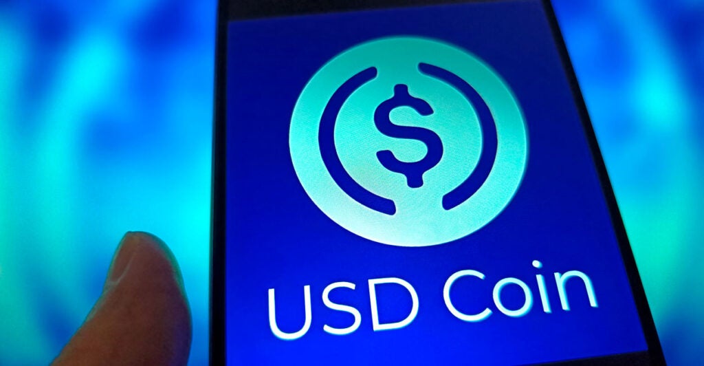 An illustration shows the USD Coin logo displayed on a smartphone.