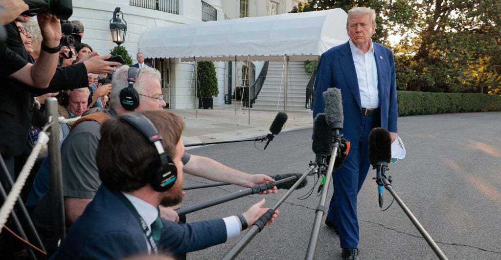 Donald Trump strolls past a group of reporters all pointing microphones at him.