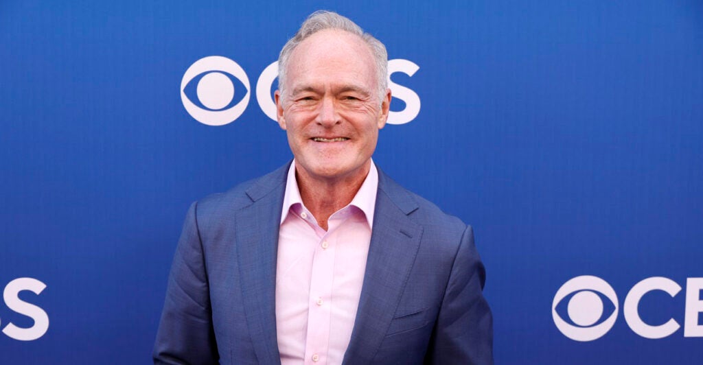 Scott Pelley stands with his hands at his side while he stands on the red carpet.