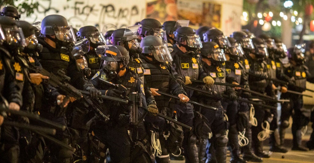Police officers stand in a row while wearing riot gear.