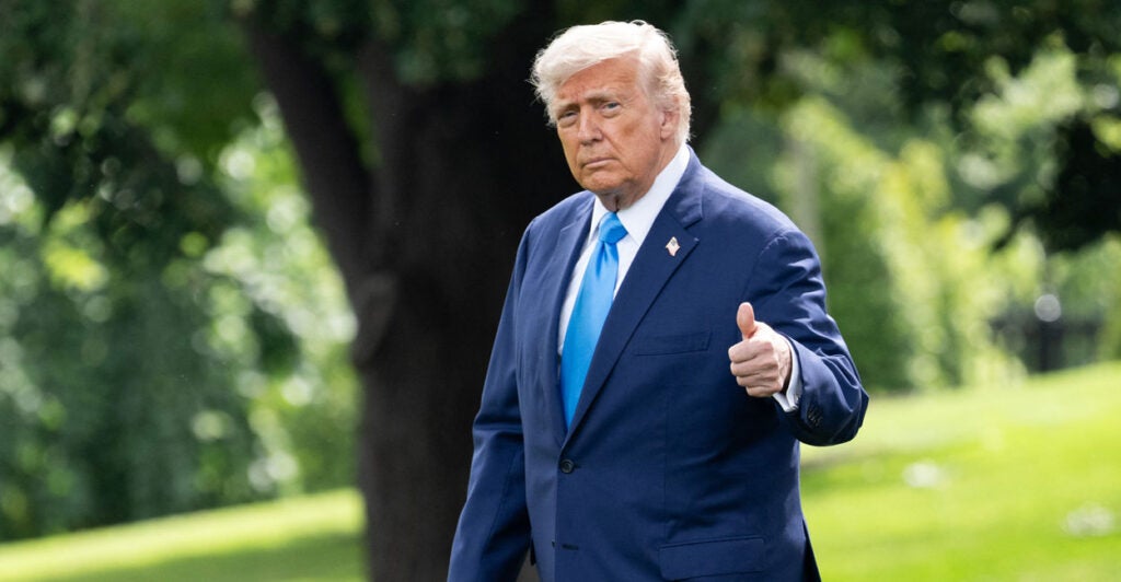 President Donald Trump walks outside in a blue suit and give a thumbs up.