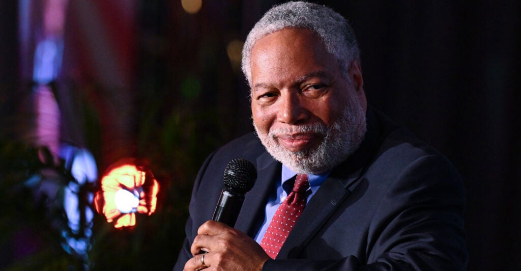 Lonnie Bunch sits while holding a microphone in his left hand as he turns his head to the left.