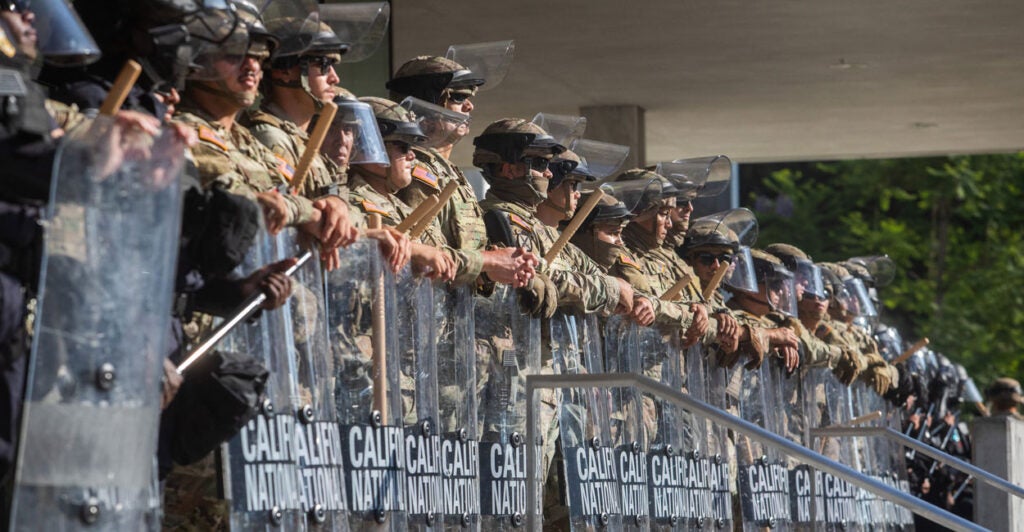 A line of California National Guard soldiers stands with batons and shields.