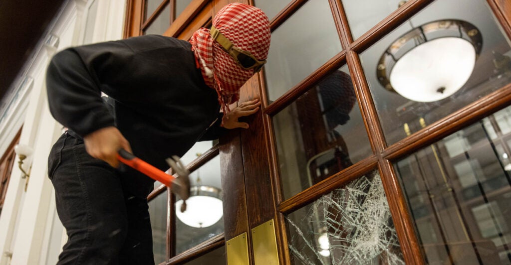 A masked protester in black smashes door glass at Columbia Univ.