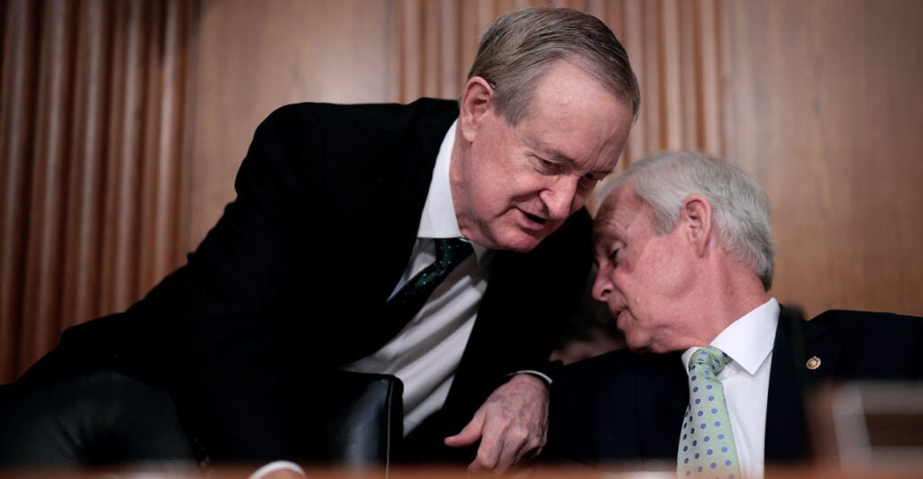 Senate Finance Committee Chair Mike Crap, standing, leans over to talk to Sen. Ron Johnson during a Senate hearing.