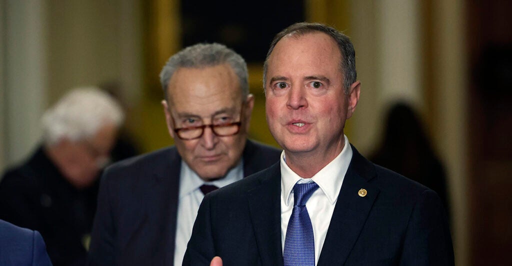 Adam Schiff in a black suit with Chuck Schumer behind him