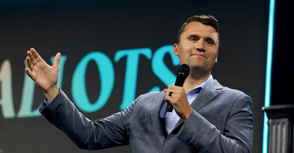 Turning Point USA Founder Charlie Kirk in a grey suit gestures with a microphone