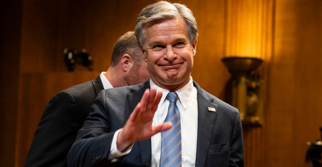Christopher Wray in a suit waves