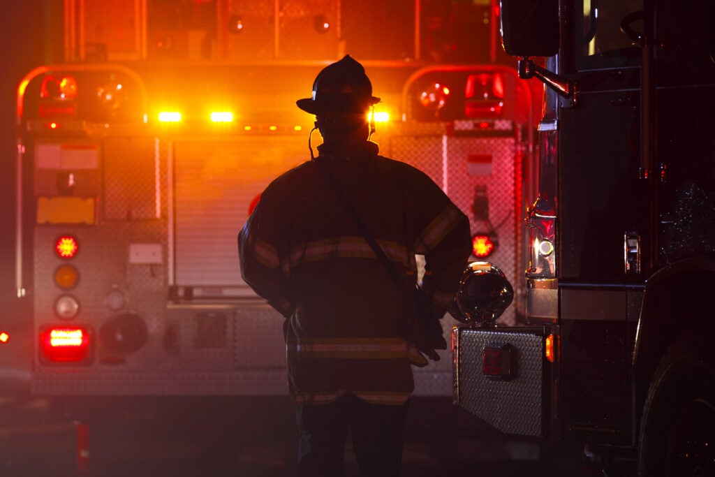 the silhouette of a firefighter in front of the lights of a fire truck on the scene