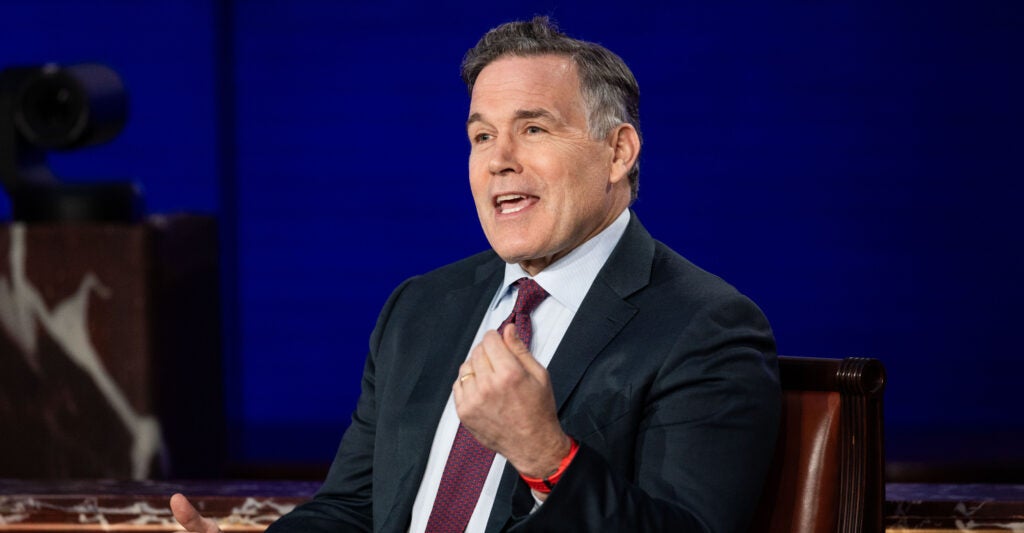 Bob Casey wears a black suit, white undershirt, and red necktie.