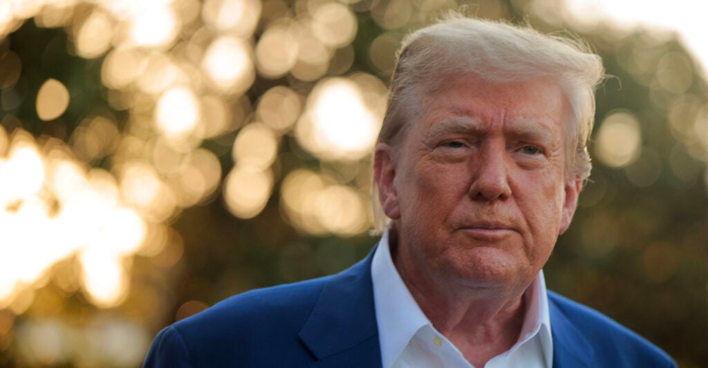 Close-up of President Trump in blue jacket and open-collar white shirt outside the White House.