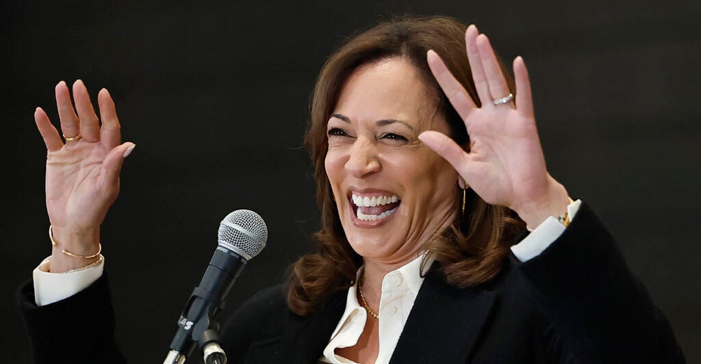 Kamala Harris wearing a black and white suit laughs and puts her hands up