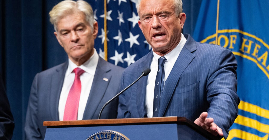 Mehmet Oz listens to RFK Jr. speak at a news conference discussing health insurance.