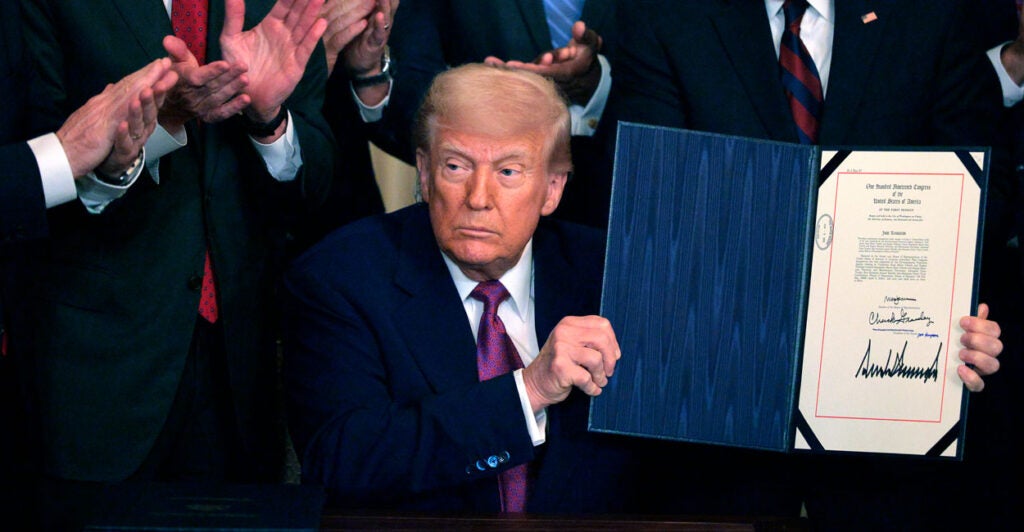 President Donald Trump holds up a signed executive order, as people around him applaud.