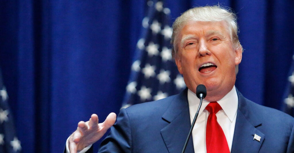 Donald Trump announcing his presidential candidacy in 2015, with American flags as a backdrop.