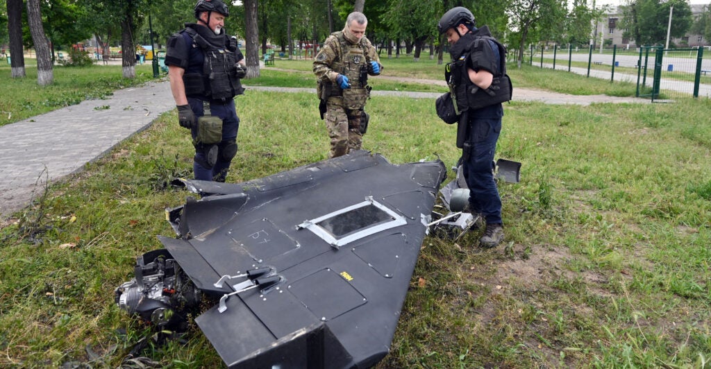Ukrainian explosives experts and police officers examine parts of a Shahed 136 military drone.