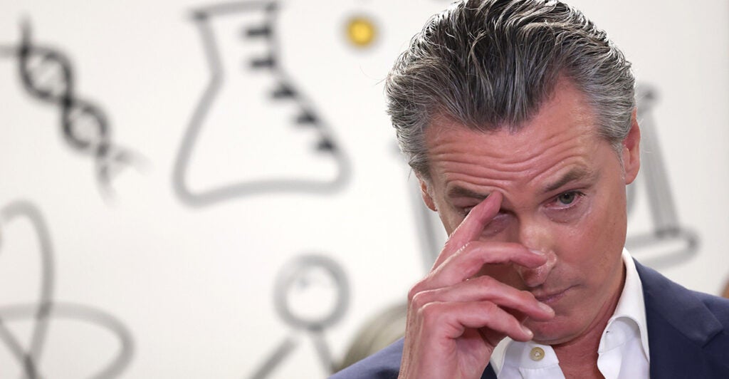 Gavin Newsom, with his hand on his face against a white backdrop with outline drawings of a beaker, DNA strands and other scientific items.