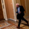 Bernie Sanders runs down a hallway holding a bag in his hand.