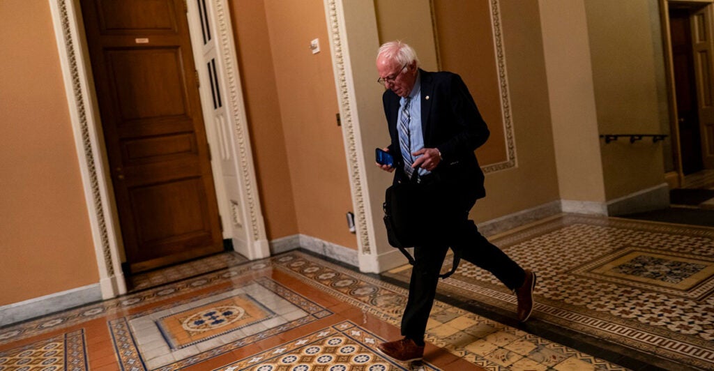 Bernie Sanders runs down a hallway holding a bag in his hand.