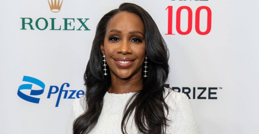 Abby Phillip poses on the red card while wearing a white dress with earrings.