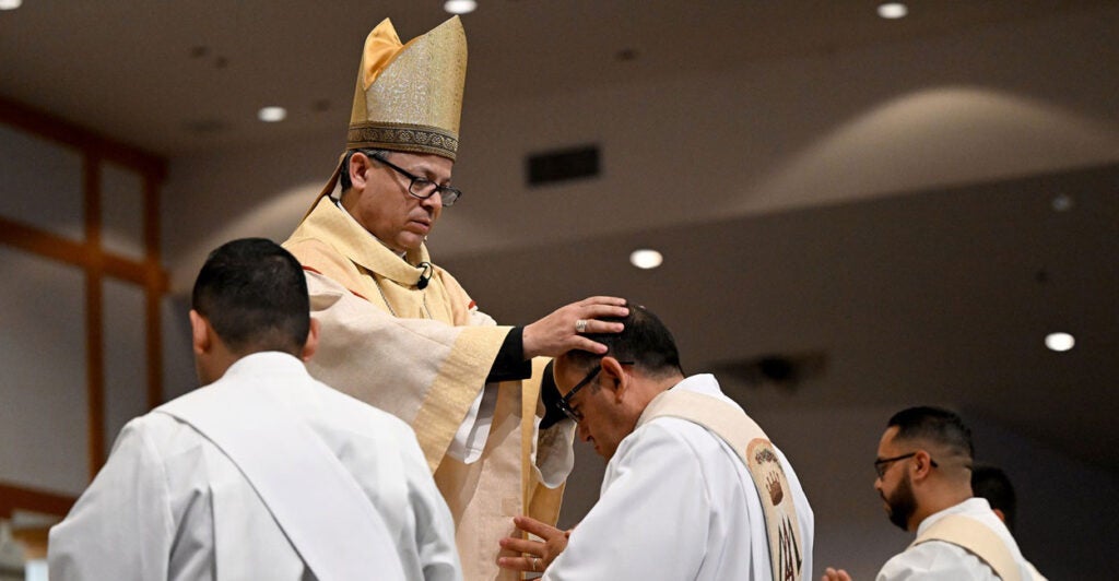 Reverend Alberto Rojas puts his hands on the head of a priest who is kneeling before him during a religious ceremony.